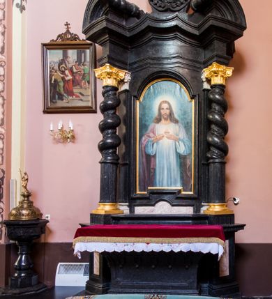 Zdjęcie nr 5: Ołtarz prostopadłościenny, w typie tumbowym, z mensą o brzegu zdobionym rzędem liści akantu naprzemian z łukami kotarowymi zwieńczonymi kulami oraz podwieszonym lambrekinem. Nastawa ołtarzowa jest architektoniczna, jednoosiowa ze zwieńczeniem, ujęta przez kolumny stojące na ukośnie dostawionych cokołach. Kolumny w jednej trzeciej kanelowane w dwóch trzecich skręcone z wplecioną wicią roślinną, ze złoconym kapitelem podtrzymują przerwany przyczółek ze ślimacznicami. Belkowanie bogato profilowane nad częścią środkową jest wyłamane trzema wklęsłymi łukami. W szczycie owalny medalion z monogramem "IHS”, w obramieniu z wieńca laurowego, ślimacznim z festonami, zakończony krzyżem. W osi środkowej prostokątna wnęka w profilowanym obramieniu, zamknięta półkolistym łukiem nadwieszonym z obrazem Najświętszego Serca Jezusowego. 


