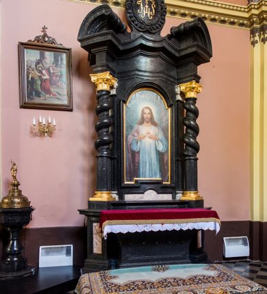 Zdjęcie nr 3: Ołtarz prostopadłościenny, w typie tumbowym, z mensą o brzegu zdobionym rzędem liści akantu naprzemian z łukami kotarowymi zwieńczonymi kulami oraz podwieszonym lambrekinem. Nastawa ołtarzowa jest architektoniczna, jednoosiowa ze zwieńczeniem, ujęta przez kolumny stojące na ukośnie dostawionych cokołach. Kolumny w jednej trzeciej kanelowane w dwóch trzecich skręcone z wplecioną wicią roślinną, ze złoconym kapitelem podtrzymują przerwany przyczółek ze ślimacznicami. Belkowanie bogato profilowane nad częścią środkową jest wyłamane trzema wklęsłymi łukami. W szczycie owalny medalion z monogramem "IHS”, w obramieniu z wieńca laurowego, ślimacznim z festonami, zakończony krzyżem. W osi środkowej prostokątna wnęka w profilowanym obramieniu, zamknięta półkolistym łukiem nadwieszonym z obrazem Najświętszego Serca Jezusowego. 


