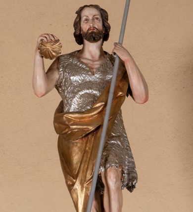 Zdjęcie nr 10: Ambona przyścienna, wisząca, z dostępem od lewej strony w postaci jednobiegowych schodów z balustradą. Kosz na planie sześcioboku na profilowanym cokole i ćwierćwałku; u spodu podwieszony profilowany ostrosłup o ściętym szczycie, zakończony szyszką. Ścianki kosza wydzielone kolumienkami  o trzonach dekorowanych do 1/3 wysokości kanelowaniem, o kapitelach korynckich, na cokołach zdobionych liśćmi akantu, dźwigającymi imposty oraz wspólny gzyms stanowiąc parapet. W polach ścianek płyciny z płaskorzeźbionymi półpostaciami czterech ewangelistów, każdy z nich ukazany został z złotej sukni, z identyfikującym go atrybutem, księgą lub zwojem i piórem w ręce –  od lewej św. Jan, św. Mateusz, św. Łukasz i św. Marek. Zaplecek w formie wydłużonego prostokąta, ujętego pilastrami podtrzymującymi imposty i wspólny gzyms. W polu płycina w formie stojącego prostokąta zamkniętego łukiem półkolistym z płaskorzeźbionym przedstawieniem Chrystusa Dobrego Pasterza, u spodu płycina z napisem „KTO WAS SŁUCHA / MNIE SŁUCHA”.  Chrystus został ukazany w całej postaci, lewą ręką podtrzymując baranka, a prawą laskę pasterską. Ma podłużna, poważną twarz, małe, niebieskie oczy, wąski nos i usta, broda dzieli się w dwa pukle; falowane włosy opadają na ramiona. Jest ubrany w długą, złotą tunikę i złoty płaszcz, na głowie ma złoty kalepusz, czerwony od wewnątrz. Stoi na trawie, u jego stóp dwa srebrzone baranki Zaplecek ujęty uszami w formie falujących liści. Baldachim powtarza kształt kosza, nakryty kopułką pokrytą łuską, z podwieszonym fryzem roślinnym, dekorowany w narożach palmetami. Baldachim stanowi podstawę dla latarni opartej na sześciu spływach wolutowych dekorowanych kampanulami, podtrzymujących belkowanie i kopułkę, stanowiącą cokół dla figury św. Jana Chrzciciela, który stoi w kontrapoście, prawą ręką unosi na wysokość twarzy muszlę, a e lewej trzyma trzyż. Ma podł€żną twarz okoczoną gęstym zarostem, wzniesiony ku górze wzrok, wąski nos i małe usta. Jest ubrany w tunikę ze srerzonego fuyta i złoty płaszcz wywiniety na prawym biodrze i przechodzący przez lewy bark. Wewnątrz latarni figura anioła na postumencie. Został ukazany w całej postaci, z rękami złożonymi na piersi. Ma okrągłą twarz o deliatnych rysach i falowane włosy opadające na kark. Jest ubrany w długa, złotą suknię w szerokomi rękawami. Z pleców wyrastają mu duże, srebrne skrzydła z ptacich piór. Na podniebiu baldachimu gołębica Ducha Świętego w glorii promienistej. Struktura polichromowana na biało, profile na czerwono, detale i ornamentyka złocone.