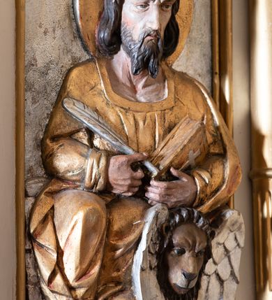 Zdjęcie nr 11: Ambona przyścienna, wisząca, z dostępem od lewej strony w postaci jednobiegowych schodów z balustradą. Kosz na planie sześcioboku na profilowanym cokole i ćwierćwałku; u spodu podwieszony profilowany ostrosłup o ściętym szczycie, zakończony szyszką. Ścianki kosza wydzielone kolumienkami  o trzonach dekorowanych do 1/3 wysokości kanelowaniem, o kapitelach korynckich, na cokołach zdobionych liśćmi akantu, dźwigającymi imposty oraz wspólny gzyms stanowiąc parapet. W polach ścianek płyciny z płaskorzeźbionymi półpostaciami czterech ewangelistów, każdy z nich ukazany został z złotej sukni, z identyfikującym go atrybutem, księgą lub zwojem i piórem w ręce –  od lewej św. Jan, św. Mateusz, św. Łukasz i św. Marek. Zaplecek w formie wydłużonego prostokąta, ujętego pilastrami podtrzymującymi imposty i wspólny gzyms. W polu płycina w formie stojącego prostokąta zamkniętego łukiem półkolistym z płaskorzeźbionym przedstawieniem Chrystusa Dobrego Pasterza, u spodu płycina z napisem „KTO WAS SŁUCHA / MNIE SŁUCHA”.  Chrystus został ukazany w całej postaci, lewą ręką podtrzymując baranka, a prawą laskę pasterską. Ma podłużna, poważną twarz, małe, niebieskie oczy, wąski nos i usta, broda dzieli się w dwa pukle; falowane włosy opadają na ramiona. Jest ubrany w długą, złotą tunikę i złoty płaszcz, na głowie ma złoty kalepusz, czerwony od wewnątrz. Stoi na trawie, u jego stóp dwa srebrzone baranki Zaplecek ujęty uszami w formie falujących liści. Baldachim powtarza kształt kosza, nakryty kopułką pokrytą łuską, z podwieszonym fryzem roślinnym, dekorowany w narożach palmetami. Baldachim stanowi podstawę dla latarni opartej na sześciu spływach wolutowych dekorowanych kampanulami, podtrzymujących belkowanie i kopułkę, stanowiącą cokół dla figury św. Jana Chrzciciela, który stoi w kontrapoście, prawą ręką unosi na wysokość twarzy muszlę, a e lewej trzyma trzyż. Ma podł€żną twarz okoczoną gęstym zarostem, wzniesiony ku górze wzrok, wąski nos i małe usta. Jest ubrany w tunikę ze srerzonego fuyta i złoty płaszcz wywiniety na prawym biodrze i przechodzący przez lewy bark. Wewnątrz latarni figura anioła na postumencie. Został ukazany w całej postaci, z rękami złożonymi na piersi. Ma okrągłą twarz o deliatnych rysach i falowane włosy opadające na kark. Jest ubrany w długa, złotą suknię w szerokomi rękawami. Z pleców wyrastają mu duże, srebrne skrzydła z ptacich piór. Na podniebiu baldachimu gołębica Ducha Świętego w glorii promienistej. Struktura polichromowana na biało, profile na czerwono, detale i ornamentyka złocone.