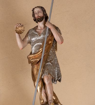 Zdjęcie nr 5: Ambona przyścienna, wisząca, z dostępem od lewej strony w postaci jednobiegowych schodów z balustradą. Kosz na planie sześcioboku na profilowanym cokole i ćwierćwałku; u spodu podwieszony profilowany ostrosłup o ściętym szczycie, zakończony szyszką. Ścianki kosza wydzielone kolumienkami  o trzonach dekorowanych do 1/3 wysokości kanelowaniem, o kapitelach korynckich, na cokołach zdobionych liśćmi akantu, dźwigającymi imposty oraz wspólny gzyms stanowiąc parapet. W polach ścianek płyciny z płaskorzeźbionymi półpostaciami czterech ewangelistów, każdy z nich ukazany został z złotej sukni, z identyfikującym go atrybutem, księgą lub zwojem i piórem w ręce –  od lewej św. Jan, św. Mateusz, św. Łukasz i św. Marek. Zaplecek w formie wydłużonego prostokąta, ujętego pilastrami podtrzymującymi imposty i wspólny gzyms. W polu płycina w formie stojącego prostokąta zamkniętego łukiem półkolistym z płaskorzeźbionym przedstawieniem Chrystusa Dobrego Pasterza, u spodu płycina z napisem „KTO WAS SŁUCHA / MNIE SŁUCHA”.  Chrystus został ukazany w całej postaci, lewą ręką podtrzymując baranka, a prawą laskę pasterską. Ma podłużna, poważną twarz, małe, niebieskie oczy, wąski nos i usta, broda dzieli się w dwa pukle; falowane włosy opadają na ramiona. Jest ubrany w długą, złotą tunikę i złoty płaszcz, na głowie ma złoty kalepusz, czerwony od wewnątrz. Stoi na trawie, u jego stóp dwa srebrzone baranki Zaplecek ujęty uszami w formie falujących liści. Baldachim powtarza kształt kosza, nakryty kopułką pokrytą łuską, z podwieszonym fryzem roślinnym, dekorowany w narożach palmetami. Baldachim stanowi podstawę dla latarni opartej na sześciu spływach wolutowych dekorowanych kampanulami, podtrzymujących belkowanie i kopułkę, stanowiącą cokół dla figury św. Jana Chrzciciela, który stoi w kontrapoście, prawą ręką unosi na wysokość twarzy muszlę, a e lewej trzyma trzyż. Ma podł€żną twarz okoczoną gęstym zarostem, wzniesiony ku górze wzrok, wąski nos i małe usta. Jest ubrany w tunikę ze srerzonego fuyta i złoty płaszcz wywiniety na prawym biodrze i przechodzący przez lewy bark. Wewnątrz latarni figura anioła na postumencie. Został ukazany w całej postaci, z rękami złożonymi na piersi. Ma okrągłą twarz o deliatnych rysach i falowane włosy opadające na kark. Jest ubrany w długa, złotą suknię w szerokomi rękawami. Z pleców wyrastają mu duże, srebrne skrzydła z ptacich piór. Na podniebiu baldachimu gołębica Ducha Świętego w glorii promienistej. Struktura polichromowana na biało, profile na czerwono, detale i ornamentyka złocone.