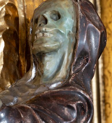 Zdjęcie nr 5: Rzeźba ścięta z tyłu, drążona, na cokole. Figura ustawiona frontalnie, w kontrapoście, z delikatnie pochyloną głową. W lewej ręce trzyma pastorał, prawą ma opuszczona, przed sobą. Twarz pociągła, o starczych rysach, z widocznymi zmarszczkami, oczy półprzymknięte, spoglądające w dół, nos prosty, usta pełne. Włosy zwinięte w pukle, głęboko. Święty ubrany w albę zapinaną na guziki, rokietę z rytą dekoracją roślinną u spodu, przepasane w talii; tkanina przylegająca do ciała, drapowana w liczne, drobne fałdki. Na piersi krzyż pektoralny i dystynktorium kanonickie. Kapa zapięta dekoracyjną fibulą, opadająca na plecy i ramiona, z kameryzowaną lamówką; tkanina sztywna, delikatnie drapowana. Na rękach czerwone rękawiczki, na głowie infuła. U lewej nogi świętego półpostać Piotrowina zwróconego profilem w lewo, ukazanego jako kościotrup, z narzuconym na czaszkę i ramiona fioletowym całunem. Polichromia naturalistyczna w odsłoniętych partiach ciała, szaty złocone, detal polichromowany.