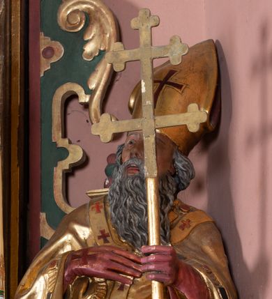 Zdjęcie nr 1: Figura drążona, na cokole. Święty Wojciech został ukazany w pozycji stojącej z uniesionymi rękami – prawą przyciska do piersi, w lewej trzyma podwójny krzyż misyjny. Twarz ma pociągłą, o wyrazistych rysach, brwi wąskie, oczy szeroko otwarte, głęboko osadzone, nos prosty, usta rozchylone. Ma długą, sięgająca dekoltu, siwiejącą brodę. Jest ubrany w sutannę, komżę oraz kapę i paliusz; na głowie ma infułę, na dłoniach czerwone rękawiczki. Paliusz i infuła zdobione czerownymi krzyżami. Polichromia w partiach ciała naturalistyczna, szaty i atrybuty złocone.