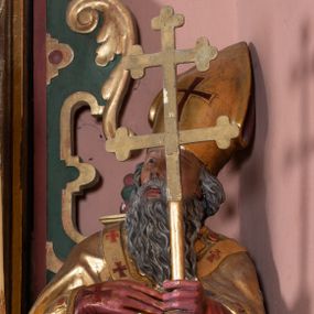 Zdjęcie nr 1: Figura drążona, na cokole. Święty Wojciech został ukazany w pozycji stojącej z uniesionymi rękami – prawą przyciska do piersi, w lewej trzyma podwójny krzyż misyjny. Twarz ma pociągłą, o wyrazistych rysach, brwi wąskie, oczy szeroko otwarte, głęboko osadzone, nos prosty, usta rozchylone. Ma długą, sięgająca dekoltu, siwiejącą brodę. Jest ubrany w sutannę, komżę oraz kapę i paliusz; na głowie ma infułę, na dłoniach czerwone rękawiczki. Paliusz i infuła zdobione czerownymi krzyżami. Polichromia w partiach ciała naturalistyczna, szaty i atrybuty złocone.