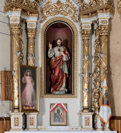 Zdjęcie nr 2: Nastawa ołtarzowa architektoniczna, jednoosiowa, jednokondygnacyjna ze zwieńczeniem. Ołtarz drewniany, prostopadłościenny. Mensa prostopadłościenna, z antepedium dekorowanym płyciną w kształcie leżącego prostokąta z krzyżem greckim o ramionach zakończonych rombami, na tle rombu i ujętym liśćmi. Flankują ją z każdej strony trzy pilastry o żłobkowanych trzonach. Na mensie, na cokole obrazem z przedstawieniem Matki Boskiej Częstochowskiejj. Nastawa ujęta parami kolumn na cokołach, z których zewnętrzne są wysunięte. Podpory dźwigają pełne belkowanie, którego architraw i fryz tworzą zygzak, w gzyms jest prosty. Na nich wspierają się trzy równoległe, załamane przyczółki zakomponowane uskokowo. Szczyt tworzy krzyż łaciński stylizowany na kwiat osadzony na łodydze z liśćmi. Pole środkowe ujęte profilowaną ramą z półokrągłą niszą wypełnioną figurą Najświętszego Serca Jezusa. Cokoły kolumn dekorowane płycinami z plakietami roślinnymi, trzony kolumn uskrzydlonymi główkami anielskimi podtrzymującymi festony utworzone z tkaniny i chwosty, między kolumnami ażurowa wić akantowa. Belkowanie ozdabia kostkowanie i astragal, pole nad obrazem wypełnia symetryczna wić akantowa, która wieńczy również gzyms belkowania i zewnętrzną krawędź przyczółków. Gzyms od spodu dekorowany rozetami. Struktura polichromowana na biało i jasnoszaro, kolumny, ornamenty i dekoracje złocone, płyciny czerwone i niebieskie; fragmenty baz kolumn zielone; nisza niebieska. 