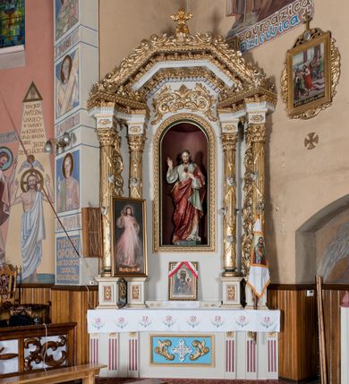 Zdjęcie nr 1: Nastawa ołtarzowa architektoniczna, jednoosiowa, jednokondygnacyjna ze zwieńczeniem. Ołtarz drewniany, prostopadłościenny. Mensa prostopadłościenna, z antepedium dekorowanym płyciną w kształcie leżącego prostokąta z krzyżem greckim o ramionach zakończonych rombami, na tle rombu i ujętym liśćmi. Flankują ją z każdej strony trzy pilastry o żłobkowanych trzonach. Na mensie, na cokole obrazem z przedstawieniem Matki Boskiej Częstochowskiejj. Nastawa ujęta parami kolumn na cokołach, z których zewnętrzne są wysunięte. Podpory dźwigają pełne belkowanie, którego architraw i fryz tworzą zygzak, w gzyms jest prosty. Na nich wspierają się trzy równoległe, załamane przyczółki zakomponowane uskokowo. Szczyt tworzy krzyż łaciński stylizowany na kwiat osadzony na łodydze z liśćmi. Pole środkowe ujęte profilowaną ramą z półokrągłą niszą wypełnioną figurą Najświętszego Serca Jezusa. Cokoły kolumn dekorowane płycinami z plakietami roślinnymi, trzony kolumn uskrzydlonymi główkami anielskimi podtrzymującymi festony utworzone z tkaniny i chwosty, między kolumnami ażurowa wić akantowa. Belkowanie ozdabia kostkowanie i astragal, pole nad obrazem wypełnia symetryczna wić akantowa, która wieńczy również gzyms belkowania i zewnętrzną krawędź przyczółków. Gzyms od spodu dekorowany rozetami. Struktura polichromowana na biało i jasnoszaro, kolumny, ornamenty i dekoracje złocone, płyciny czerwone i niebieskie; fragmenty baz kolumn zielone; nisza niebieska. 