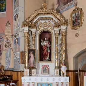 Zdjęcie nr 1: Nastawa ołtarzowa architektoniczna, jednoosiowa, jednokondygnacyjna ze zwieńczeniem. Ołtarz drewniany, prostopadłościenny. Mensa prostopadłościenna, z antepedium dekorowanym płyciną w kształcie leżącego prostokąta z krzyżem greckim o ramionach zakończonych rombami, na tle rombu i ujętym liśćmi. Flankują ją z każdej strony trzy pilastry o żłobkowanych trzonach. Na mensie, na cokole obrazem z przedstawieniem Matki Boskiej Częstochowskiejj. Nastawa ujęta parami kolumn na cokołach, z których zewnętrzne są wysunięte. Podpory dźwigają pełne belkowanie, którego architraw i fryz tworzą zygzak, w gzyms jest prosty. Na nich wspierają się trzy równoległe, załamane przyczółki zakomponowane uskokowo. Szczyt tworzy krzyż łaciński stylizowany na kwiat osadzony na łodydze z liśćmi. Pole środkowe ujęte profilowaną ramą z półokrągłą niszą wypełnioną figurą Najświętszego Serca Jezusa. Cokoły kolumn dekorowane płycinami z plakietami roślinnymi, trzony kolumn uskrzydlonymi główkami anielskimi podtrzymującymi festony utworzone z tkaniny i chwosty, między kolumnami ażurowa wić akantowa. Belkowanie ozdabia kostkowanie i astragal, pole nad obrazem wypełnia symetryczna wić akantowa, która wieńczy również gzyms belkowania i zewnętrzną krawędź przyczółków. Gzyms od spodu dekorowany rozetami. Struktura polichromowana na biało i jasnoszaro, kolumny, ornamenty i dekoracje złocone, płyciny czerwone i niebieskie; fragmenty baz kolumn zielone; nisza niebieska. 