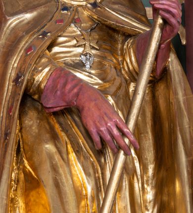 Zdjęcie nr 16: Nastawa ołtarzowa architektoniczna, jednoosiowa, jednokondygnacyjna ze zwieńczeniem. Ołtarz drewniany, prostopadłościenny. Mensa drewniana, o silnie wysuniętym gzymsie dekorowanego kostkowaniem. Antepedium w formie leżącego prostokąta z płyciną o dwóch wypukłych bokach. W polu płaskorzeźbione przedstawienie pelikana karmiącego w gnieździe młode, flankowanego winnym gronem i kłosami zbóż; płycina ujęta parą uskrzydlonych główek anielskich. Antepedium zamknięte profilowanym gzymsem, dekorowanym kostkowaniem, dźwigającym niepełne belkowanie. Tabernakulum prostopadłościenne, w formie drewnianej skrzynki obitej blachą miedzianą, ustawione na wysokim cokole ujętym od frontu i po bokach spływami wolutowymi, dźwigającymi wyłamany gzyms dekorowany kostkowaniem; na froncie płycina z rozetą. Drzwiczki w kształcie leżącego prostokąta zamkniętego łukiem segmentowym z aplikowanym kielichem z hostią, w otoczeniu winnego grona, na fakturowanym tle. Tabernakulum flankowane parą kanelowanych kolumienek, dźwigających gzyms wieńczący, dekorowany kostkowaniem oraz szczyt w formie zbliżonej do trójkąta, zamknięty gzymsem przechodzącym w przeciwstawnie zwrócone woluty, dekorowane kostkowaniem; w polu uskrzydlona główka anielska. 
Retabulum na zryzalitowanym przy brzegach cokole; ujęte dwiema parami kolumn o kapitelach kompozytowych i kanelowanych trzonach dźwigających pełne belkowanie oraz trójkątny przyczółek trójbocznie załamany; na nim, na osi podpór przerwany, wolutowy przyczółek, z leżącymi nań figurami. Szczyt w postaci dwustrefowego cokołu ujętego kartuszem z figurą św. Michała Archanioła. Pole środkowe w całości wypełnia płytka nisza ujęta profilowaną ramą z obrazem „Trójca Święta”, wymiennie z przedstawieniami Matki Boskiej z Dzieciątkiem i św. Katarzyny. Kondygnację flankują, ustawione na cokołach figury św. Stanisława i św. Wojciecha. Cokoły kolumn dekorowane płycinami z uskrzydlonymi główkami anielskimi; w polu cokołu płycina w formie wydłużonego, leżącego prostokąta o wypukłych bokach, z dekoracją schweifwerkową. Trzony kolumn dekorowane uskrzydlonymi główkami anielskimi podtrzymującymi festony utworzone z tkaniny i chwosty. Za kolumnami płyciny wypełnione schweifwerkiem, w ich centrum obelisk dekorowany cekinami i zwieńczony krzyżem. W partii fryzu od frontu uskrzydlone główki anielskie, po bokach schweifwerk. Pola obu przyczółków wypełnia ornament schweifwerkowy. Gzyms od spodu dekorowany rozetami; zwieńczony wolutowym kluczem dekorowanym schwrifwerkiem oraz uskrzydloną główką anielską. Woluty wieńczące zdobione palmetami. Kondygnacja ujęta uszami utworzonymi z ornamentu okuciowego i ulistnionych wolut. Struktura w całości złocona, płyciny i profile polichromowane na czerwono, uszaki na zielono. 