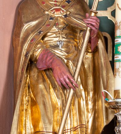 Zdjęcie nr 15: Nastawa ołtarzowa architektoniczna, jednoosiowa, jednokondygnacyjna ze zwieńczeniem. Ołtarz drewniany, prostopadłościenny. Mensa drewniana, o silnie wysuniętym gzymsie dekorowanego kostkowaniem. Antepedium w formie leżącego prostokąta z płyciną o dwóch wypukłych bokach. W polu płaskorzeźbione przedstawienie pelikana karmiącego w gnieździe młode, flankowanego winnym gronem i kłosami zbóż; płycina ujęta parą uskrzydlonych główek anielskich. Antepedium zamknięte profilowanym gzymsem, dekorowanym kostkowaniem, dźwigającym niepełne belkowanie. Tabernakulum prostopadłościenne, w formie drewnianej skrzynki obitej blachą miedzianą, ustawione na wysokim cokole ujętym od frontu i po bokach spływami wolutowymi, dźwigającymi wyłamany gzyms dekorowany kostkowaniem; na froncie płycina z rozetą. Drzwiczki w kształcie leżącego prostokąta zamkniętego łukiem segmentowym z aplikowanym kielichem z hostią, w otoczeniu winnego grona, na fakturowanym tle. Tabernakulum flankowane parą kanelowanych kolumienek, dźwigających gzyms wieńczący, dekorowany kostkowaniem oraz szczyt w formie zbliżonej do trójkąta, zamknięty gzymsem przechodzącym w przeciwstawnie zwrócone woluty, dekorowane kostkowaniem; w polu uskrzydlona główka anielska. 
Retabulum na zryzalitowanym przy brzegach cokole; ujęte dwiema parami kolumn o kapitelach kompozytowych i kanelowanych trzonach dźwigających pełne belkowanie oraz trójkątny przyczółek trójbocznie załamany; na nim, na osi podpór przerwany, wolutowy przyczółek, z leżącymi nań figurami. Szczyt w postaci dwustrefowego cokołu ujętego kartuszem z figurą św. Michała Archanioła. Pole środkowe w całości wypełnia płytka nisza ujęta profilowaną ramą z obrazem „Trójca Święta”, wymiennie z przedstawieniami Matki Boskiej z Dzieciątkiem i św. Katarzyny. Kondygnację flankują, ustawione na cokołach figury św. Stanisława i św. Wojciecha. Cokoły kolumn dekorowane płycinami z uskrzydlonymi główkami anielskimi; w polu cokołu płycina w formie wydłużonego, leżącego prostokąta o wypukłych bokach, z dekoracją schweifwerkową. Trzony kolumn dekorowane uskrzydlonymi główkami anielskimi podtrzymującymi festony utworzone z tkaniny i chwosty. Za kolumnami płyciny wypełnione schweifwerkiem, w ich centrum obelisk dekorowany cekinami i zwieńczony krzyżem. W partii fryzu od frontu uskrzydlone główki anielskie, po bokach schweifwerk. Pola obu przyczółków wypełnia ornament schweifwerkowy. Gzyms od spodu dekorowany rozetami; zwieńczony wolutowym kluczem dekorowanym schwrifwerkiem oraz uskrzydloną główką anielską. Woluty wieńczące zdobione palmetami. Kondygnacja ujęta uszami utworzonymi z ornamentu okuciowego i ulistnionych wolut. Struktura w całości złocona, płyciny i profile polichromowane na czerwono, uszaki na zielono. 