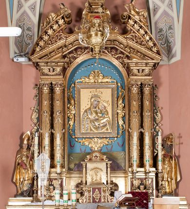 Zdjęcie nr 2: Nastawa ołtarzowa architektoniczna, jednoosiowa, jednokondygnacyjna ze zwieńczeniem. Ołtarz drewniany, prostopadłościenny. Mensa drewniana, o silnie wysuniętym gzymsie dekorowanego kostkowaniem. Antepedium w formie leżącego prostokąta z płyciną o dwóch wypukłych bokach. W polu płaskorzeźbione przedstawienie pelikana karmiącego w gnieździe młode, flankowanego winnym gronem i kłosami zbóż; płycina ujęta parą uskrzydlonych główek anielskich. Antepedium zamknięte profilowanym gzymsem, dekorowanym kostkowaniem, dźwigającym niepełne belkowanie. Tabernakulum prostopadłościenne, w formie drewnianej skrzynki obitej blachą miedzianą, ustawione na wysokim cokole ujętym od frontu i po bokach spływami wolutowymi, dźwigającymi wyłamany gzyms dekorowany kostkowaniem; na froncie płycina z rozetą. Drzwiczki w kształcie leżącego prostokąta zamkniętego łukiem segmentowym z aplikowanym kielichem z hostią, w otoczeniu winnego grona, na fakturowanym tle. Tabernakulum flankowane parą kanelowanych kolumienek, dźwigających gzyms wieńczący, dekorowany kostkowaniem oraz szczyt w formie zbliżonej do trójkąta, zamknięty gzymsem przechodzącym w przeciwstawnie zwrócone woluty, dekorowane kostkowaniem; w polu uskrzydlona główka anielska. 
Retabulum na zryzalitowanym przy brzegach cokole; ujęte dwiema parami kolumn o kapitelach kompozytowych i kanelowanych trzonach dźwigających pełne belkowanie oraz trójkątny przyczółek trójbocznie załamany; na nim, na osi podpór przerwany, wolutowy przyczółek, z leżącymi nań figurami. Szczyt w postaci dwustrefowego cokołu ujętego kartuszem z figurą św. Michała Archanioła. Pole środkowe w całości wypełnia płytka nisza ujęta profilowaną ramą z obrazem „Trójca Święta”, wymiennie z przedstawieniami Matki Boskiej z Dzieciątkiem i św. Katarzyny. Kondygnację flankują, ustawione na cokołach figury św. Stanisława i św. Wojciecha. Cokoły kolumn dekorowane płycinami z uskrzydlonymi główkami anielskimi; w polu cokołu płycina w formie wydłużonego, leżącego prostokąta o wypukłych bokach, z dekoracją schweifwerkową. Trzony kolumn dekorowane uskrzydlonymi główkami anielskimi podtrzymującymi festony utworzone z tkaniny i chwosty. Za kolumnami płyciny wypełnione schweifwerkiem, w ich centrum obelisk dekorowany cekinami i zwieńczony krzyżem. W partii fryzu od frontu uskrzydlone główki anielskie, po bokach schweifwerk. Pola obu przyczółków wypełnia ornament schweifwerkowy. Gzyms od spodu dekorowany rozetami; zwieńczony wolutowym kluczem dekorowanym schwrifwerkiem oraz uskrzydloną główką anielską. Woluty wieńczące zdobione palmetami. Kondygnacja ujęta uszami utworzonymi z ornamentu okuciowego i ulistnionych wolut. Struktura w całości złocona, płyciny i profile polichromowane na czerwono, uszaki na zielono. 