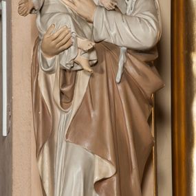 Zdjęcie nr 1: Rzeźba pełnoplastyczna, ustawiona na profilowanej podstawie na planie kwadratu o ściętych narożach. Józef ustawiony jest frontalnie, w kontrapoście, z lekko pochyloną głową. Na prawym przedramieniu podtrzymuje siedzące Dzieciątko, lewym przedramieniem przyciska do ciała gałązkę lilii, kładąc dłoń na piersi Dzieciątka. Twarz świętego jest pociągła, z wysokim czołem, o delikatnych rysach, małych oczach skierowanych w dół i prostym nosie, okolona krótką brodą i krótkimi kręconymi włosami. Ubrany jest w białą tunikę oraz jasnobrązowy płaszcz z beżową podszewką zarzucony na prawe ramię i otaczający postać. Dzieciątko skierowane jest w trzech czwartych w lewo, ma pochyloną głowę i rozłożone na boki ręce. Twarz ma okrągłą o pełnych policzkach i delikatnych rysach, okoloną krótkimi, kręconymi włosami. Ubrane jest w białą, luźną tunikę. Polichromia ciała naturalistyczna. 