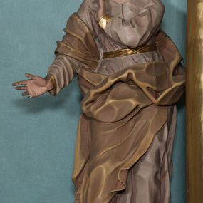 Zdjęcie nr 1: Rzeźba drążona, ustawiona na niewielkiej podstawie na planie kwadratu. Figura ukazana frontalnie, w kontrapoście, z głową przechyloną na prawy bark. Lewą rękę ma ugiętą przy piersi, prawą wyciąga w bok. Twarz ma pociągłą, o starczych rysach, dużych oczach, lekko garbatym nosie i niewielkich ustach, okoloną długimi włosami, zakrytymi welonem. Ubrana jest w bladoróżową tunikę o pozłoconych brzegach rękawów, przepasaną pozłoconą szarfą, silnie drapowaną oraz jasnobrązowy płaszcz zawinięty na prawym ramieniu i otaczający postać w partii bioder, o ekspresyjnie kształtowanej tkaninie. Na głowie ma jasnobrązowy welon opadający na plecy. Polichromia ciała naturalistyczna. 