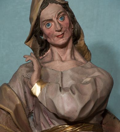 Zdjęcie nr 2: Rzeźba drążona, ustawiona na niewielkiej podstawie na planie kwadratu. Figura ukazana frontalnie, w kontrapoście, z głową przechyloną na prawy bark. Lewą rękę ma ugiętą przy piersi, prawą wyciąga w bok. Twarz ma pociągłą, o starczych rysach, dużych oczach, lekko garbatym nosie i niewielkich ustach, okoloną długimi włosami, zakrytymi welonem. Ubrana jest w bladoróżową tunikę o pozłoconych brzegach rękawów, przepasaną pozłoconą szarfą, silnie drapowaną oraz jasnobrązowy płaszcz zawinięty na prawym ramieniu i otaczający postać w partii bioder, o ekspresyjnie kształtowanej tkaninie. Na głowie ma jasnobrązowy welon opadający na plecy. Polichromia ciała naturalistyczna. 