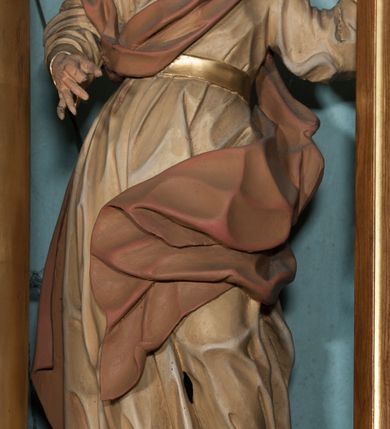Zdjęcie nr 2: Rzeźba drążona, ustawiona na niewysokiej podstawie o nieregularnym kształcie. Figura zwrócona w trzech czwartych w prawo, w kontrapoście, sylwetka silnie odchylona w tył, z głową skierowaną do góry. Prawa ręka ugięta, znajduje się przed klatką piersiową, lewa wyciągnięta jest w lewo i w górę. Twarz ma pociągłą, o skierowanych w górę oczach, lekko garbatym nosie i otwartych ustach, okolona jest wysuniętą w przód, gęstą, kręconą brodą oraz krótkimi włosami rzeźbionymi w pojedyncze pukle. Święty ubrany jest w beżową tunikę o pozłoconych mankietach i pasie w talii oraz pozłacane nakrycie głowy. Przez klatkę piersiową i prawe ramię przerzucony jest fragment czerwono-brązowego, silnie drapowanego płaszcza, który opada na plecy i lewą nogę. Polichromia ciała naturalistyczna. 