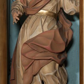 Zdjęcie nr 1: Rzeźba drążona, ustawiona na niewysokiej podstawie o nieregularnym kształcie. Figura zwrócona w trzech czwartych w prawo, w kontrapoście, sylwetka silnie odchylona w tył, z głową skierowaną do góry. Prawa ręka ugięta, znajduje się przed klatką piersiową, lewa wyciągnięta jest w lewo i w górę. Twarz ma pociągłą, o skierowanych w górę oczach, lekko garbatym nosie i otwartych ustach, okolona jest wysuniętą w przód, gęstą, kręconą brodą oraz krótkimi włosami rzeźbionymi w pojedyncze pukle. Święty ubrany jest w beżową tunikę o pozłoconych mankietach i pasie w talii oraz pozłacane nakrycie głowy. Przez klatkę piersiową i prawe ramię przerzucony jest fragment czerwono-brązowego, silnie drapowanego płaszcza, który opada na plecy i lewą nogę. Polichromia ciała naturalistyczna. 