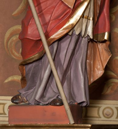 Zdjęcie nr 2: Rzeźba drążona, ustawiona na podstawie na planie prostokąta. Figura zwrócona jest w trzech czwartych w lewo, w delikatnym kontrapoście, o łukowato wygiętej sylwetce. W prawej, ugiętej ręce trzyma pastorał, lewą wyciąga przed siebie. Twarz ma pociągłą, szczupłą, z silnie zaznaczonymi łukami brwiowymi i kośćmi policzkowymi, z szeroko otwartymi oczami, prostym nosem i otwartymi ustami, okoloną bujną, kręconą brodą oraz krótkimi, kręconymi włosami. Święty jest ubrany w fioletową albę, białą rokietę ze złotą lamówką u szyi oraz czerwoną kapę ze złotą lamówką i pomarańczową podszewką, zapiętą na piersi, opadającą na plecy, z zawiniętym i ekspresyjnie rozwianym fragmentem tkaniny na prawej nodze. Na głowie wysoka infuła z pozłoconym krzyżem i brzegami. Polichromia naturalistyczna w partiach ciała. 