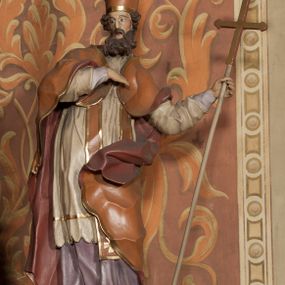 Zdjęcie nr 1: Rzeźba drążona, ustawiona na niskiej podstawie na planie prostokąta. Figura zwrócona jest w trzech czwartych w prawo, w delikatnym kontrapoście, o łukowatym układzie sylwetki, odchylona w tył. Prawa ręka skierowana na pierś, w lewej, ugiętej ferula. Twarz ma pociągłą, szczupłą, z wyraźnie zaznaczonymi kośćmi policzkowymi i łukami brwiowymi, z głęboko osadzonymi oczami, prostym nosem i otwartymi ustami, okoloną długą, falowaną i gęstą brodą. Włosy krótkie, kręcone, opadające na tył głowy. Święty ubrany jest w fioletową albę, białą rokietę, długą pomarańczową stułę z pozłacanymi brzegami oraz pomarańczową kapę z ciemnoróżową podszewką, zapiętą na piersi, opadającą na plecy, z rozwianym i zawiniętym na lewej nodze fragmentem tkaniny. Na głowie wysoka pomarańczowa infuła z pozłacanym krzyżem i brzegami. Polichromia ciała naturalistyczna. 