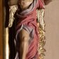 Zdjęcie nr 1: Rzeźba ścięta z tyłu, drążona, przedstawia anioła stojącego na  rzeźbionym, posrebrzanym obłoku. Figura zwrócona frontalnie, z prawą nogą opartą na obłoku, głową przechyloną na prawy bark oraz uniesionymi przed sobą, ugiętymi rękami. Twarz owalna, o pełnych policzkach i wystającej brodzie, migdałowatych, opadających oczach, małym nosie i ustach, okolona krótkimi, zaczesanymi do tyłu włosami. Anioł ubrany jest w silnie fałdowaną, różową tunikę z fioletową podszewką, z jednym rękawem na lewym przedramieniu, odsłaniającą połowę torsu i prawe ramię oraz prawą nogę. Skrzydła pozłocone, złożone po bokach postaci. Polichromia ciała naturalistyczna. 

