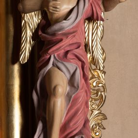 Zdjęcie nr 1: Rzeźba ścięta z tyłu, drążona, przedstawia anioła stojącego na  rzeźbionym, posrebrzanym obłoku. Figura zwrócona frontalnie, z prawą nogą opartą na obłoku, głową przechyloną na prawy bark oraz uniesionymi przed sobą, ugiętymi rękami. Twarz owalna, o pełnych policzkach i wystającej brodzie, migdałowatych, opadających oczach, małym nosie i ustach, okolona krótkimi, zaczesanymi do tyłu włosami. Anioł ubrany jest w silnie fałdowaną, różową tunikę z fioletową podszewką, z jednym rękawem na lewym przedramieniu, odsłaniającą połowę torsu i prawe ramię oraz prawą nogę. Skrzydła pozłocone, złożone po bokach postaci. Polichromia ciała naturalistyczna. 

