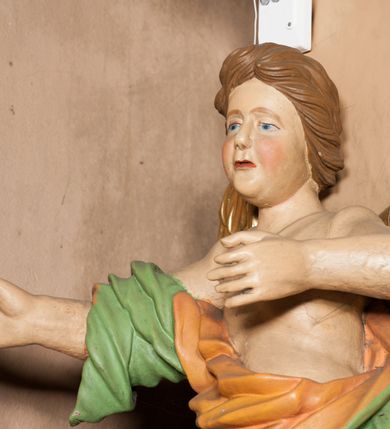 Zdjęcie nr 2: Rzeźba ścięta z tyłu, drążona, ustawiona na rzeźbionym, posrebrzanym obłoku. Figura anioła ukazana frontalnie, z lewą nogą opartą na obłoku oraz wyciągniętymi przed siebie, ugiętymi rękoma. Twarz ma owalną, o pełnych policzkach i podkreślonej brodzie, migdałowatych, opadających oczach, małym nosie i ustach, okoloną krótkimi, falowanymi, zaczesanymi w tył włosami. Anioł ubrany jest w obficie fałdowaną zieloną tunikę z pomarańczową podszewką, z jednym rękawem na prawym ramieniu, odsłaniającą tors, lewe ramię oraz lewą nogę. Skrzydła pozłacane, złożone po bokach postaci. Polichromia ciała naturalistyczna. 
