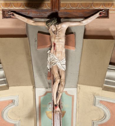 Zdjęcie nr 1: Figura umarłego Chrystusa przybita do krzyża o prostych ramionach trzema gwoździami. Ciało w lekkim zwisie o horyzontalnie rozłożonych ramionach, głowie opadającej bezwładnie w prawą stronę, z lekko ugiętymi w kolanach nogami oraz stopami skrzyżowanymi w układzie prawa na lewą. Twarz szczupła, pociągła, z zamkniętymi oczami, długim, wąskim nosem i otwartymi ustami, okolona krótką brodą skręconą w regularne pukle oraz falowanymi włosami opadającymi na plecy i prawe ramię. Na głowie ma zieloną koronę cierniową w formie kołpaka. Sylwetka smukła, proporcjonalnie wydłużona, ciało silnie wychudzone o podkreślonych mięśniach, żebrach i mostku klatki piersiowej oraz ścięgnach nóg i rąk. W boku zaznaczona rana z rzeźbionymi kroplami krwi. Perizonium   białe, krótkie, ściśle przylegające do ciała, silnie drapowane, odwinięte i osuwające się w partii podbrzusza, z kaskadowym zwisem tkaniny na prawym boku. Polichromia ciała naturalistyczna z zaznaczonymi śladami męki. Do górnej belki krzyża przybita płaskorzeźbiona tabliczka z inskrypcją „INRI”. 