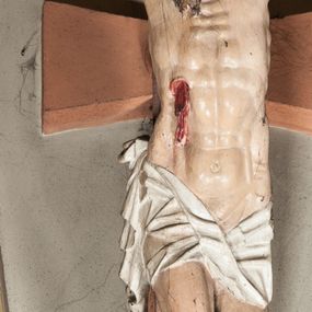 Zdjęcie nr 1: Figura umarłego Chrystusa przybita do krzyża o prostych ramionach trzema gwoździami. Ciało w lekkim zwisie o horyzontalnie rozłożonych ramionach, głowie opadającej bezwładnie w prawą stronę, z lekko ugiętymi w kolanach nogami oraz stopami skrzyżowanymi w układzie prawa na lewą. Twarz szczupła, pociągła, z zamkniętymi oczami, długim, wąskim nosem i otwartymi ustami, okolona krótką brodą skręconą w regularne pukle oraz falowanymi włosami opadającymi na plecy i prawe ramię. Na głowie ma zieloną koronę cierniową w formie kołpaka. Sylwetka smukła, proporcjonalnie wydłużona, ciało silnie wychudzone o podkreślonych mięśniach, żebrach i mostku klatki piersiowej oraz ścięgnach nóg i rąk. W boku zaznaczona rana z rzeźbionymi kroplami krwi. Perizonium   białe, krótkie, ściśle przylegające do ciała, silnie drapowane, odwinięte i osuwające się w partii podbrzusza, z kaskadowym zwisem tkaniny na prawym boku. Polichromia ciała naturalistyczna z zaznaczonymi śladami męki. Do górnej belki krzyża przybita płaskorzeźbiona tabliczka z inskrypcją „INRI”. 