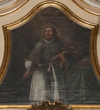 Zdjęcie nr 1: Obraz w formie trapezu o wklęsłych bokach, zamknięty faliście. W centrum kompozycji św. Jan Nepomucen ukazany do wysokości kolan, zwrócony frontalnie, z głową uniesioną do góry. Obiema rękami przytrzymuje krucyfiks oparty na jego lewym ramieniu. Twarz ma pociągłą, szczupłą, o rysach wydobytych głębokim światłocieniem, z oczami skierowanymi do góry, prostym nosem i pełnymi ustami, okoloną bujną brodą oraz włosami sięgającymi ramion. Wokół głowy świętego nimb i wieniec z pięciu gwiazd. Jan Nepomucen ubrany jest w białą komżę z wąskimi rękawami, lamowaną koronką, brązową almucję z różową podszewką zawiązaną u szyi niebieskim sznurem. W prawej części obrazu znajduje się stół przesłonięty zieloną tkaniną, z leżącymi na nim dwiema książkami. W górnej części dzieła ukazane ciemne niebo z zarysem obłoków, rozjaśnione wokół głowy świętego. Obraz ujęty profilowaną, pozłoconą ramą.