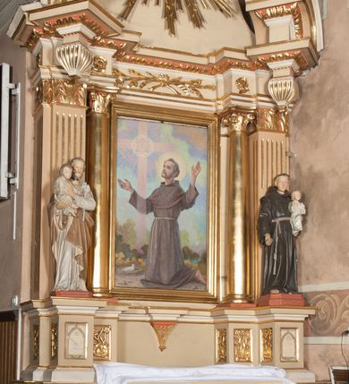Zdjęcie nr 2: Nastawa architektoniczna, jednoosiowa, jednokondygnacyjna ze zwieńczeniem, ustawiona na wysokim dwustrefowym cokole. Ołtarz drewniany, prostopadłościenny z drewnianą mensą i kamiennym portatylem. Antepedium ujęte profilowaną ramą, w polu medalion z literą omega. Retabulum ujęte dwiema parami pilastrów, przed wewnętrzną stoi para kolumn o kapitelach korynckich. Zewnętrzne pilastry zdwojone, z kanelowanym trzonem, przed nimi znajdują się figury św. Józefa z Dzieciątkiem i św. Antoniego Padewskiego z Dzieciątkiem. Podpory dźwigają pełne belkowanie, dekorowane w partii fryzu ornamentem roślinnym. Nad figurami ustawione pod kątem imposty podtrzymywane przez wazonowate wsporniki, dźwigające przerwany półkolisty przyczółek. Całe pole środkowe wypełnia płycina w formie stojącego prostokąta z obrazem św. Franciszka, podtrzymywana u dołu przez wspornik. Zwieńczenie w formie trapezu wypełnione niemal w całości owalnym medalionem z obrazem św. Antoniego Padewskiego z Dzieciątkiem i Matką Boską, ujętym otokiem z obłoków z uskrzydlonymi główkami anielskimi w glorii promienistej. Struktura ołtarza polichromowana w kolorze beżowym, ornamentyka, profile i gloria pozłacane.