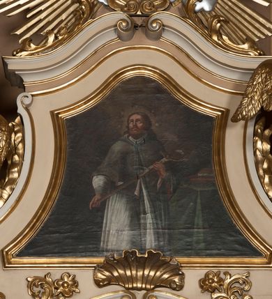 Zdjęcie nr 4: Rzeźby ścięte z tyłu, drążone, ukazane jako siedzące na przerwanym przyczółku, skierowane w stronę ołtarza. Lewa figura pochylona, z uniesioną nad głową prawą ręką i wyciągniętą przed siebie lewą. Figura anioła po prawej, lewą rękę kładzie na piersi, prawą wyciąga przed siebie. Anioły mają pociągłe twarze, z wystającymi brodami, dużymi oczami, zadartymi nosami i pełnymi ustami, okolone silnie kręconymi włosami opadającymi na kark. Anioł po lewej stronie ubrany jest w niebieską, silnie drapowaną szatę, odsłaniającą częściowo tors, przerzuconą przez prawe ramię, podtrzymywaną na lewym ramieniu wstążką, otaczającą postać w partii bioder. Anioł po prawej ubrany jest w czerwoną, ekspresyjnie fałdowaną szatę odsłaniającą tors, przerzuconą przez lewe ramię i otaczającą postać w partii bioder. Skrzydła obu aniołów rozpostarte na boki, pozłocone. Polichromia ciała naturalistyczna. 