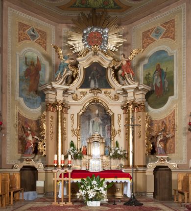 Zdjęcie nr 1: Nastawa ołtarzowa architektoniczna, jednoosiowa z bramkami, jednokondygnacyjna ze zwieńczeniem, na wysokim cokole. Ołtarz prostopadłościenny, mensa drewniana z marmurowym portatylem. Antepedium w formie leżącego prostokąta, ujęte profilowaną ramą. W jego polu trzy medaliony, w środkowym monogram IHS, w zewnętrznych alfa i omega, w narożach rocaille. Tabernakulum w formie prostopadłościennej metalowej skrzynki obitej fakturowaną blachą. Drzwiczki dwuskrzydłowe w kształcie stojącego prostokąta, w metalowych opaskach, z aplikowanymi, odlewanymi przedstawieniami krzyży ze zbożem i winnym gronem na fakturowanym tle. Tabernakulum w drewnianej obudowie stanowiącej dwustrefowy cokół dla tronu wstawienia, dekorowany płycinami z rozetami. Tron w formie obrotowej niszy w kształcie stojącego prostokąta zamkniętego łukiem półkolistym, ujętej dwiema parami kolumienek o kapitelach korynckich, dźwigających pełne belkowanie, przyjmujące nad niszą kształt łuku segmentowego o wypukłym licu. Na belkowaniu cokół ujęty w narożach spływami wolutowymi z figurą baranka apokaliptycznego na księdze.  
Nastawa flankowana dwiema parami pilastrów i parą filarów zewnętrznych ustawionych delikatnie pod kątem względem lica ołtarza, o trzonach dekorowanych rocaille&#039;m i zwisami kwiatowymi, przed nimi para kolumn o kapitelach kompozytowych. Podpory dźwigają pełne belkowanie, wyłamane na ich osi oraz przerwany, wolutowy przyczółek z figurami aniołów. Belkowanie przerwane nad polem środkowym, połączone architrawem przyjmującym kształt łuku nadwieszonego. W polu środkowym nisza w formie stojącego prostokąta zamkniętego łukiem półkolistym nadwieszonym z uskokiem z obrazem św. Stanisława, ujęta profilowaną ramą dekorowaną rocaille&#039;m. Nisza flankowana rocaille&#039;m i zwisami kwiatowymi. Kondygnacja ujęta uszami utworzonymi z rocaille&#039;u, wolut i dekoracji roślinnej. Zwieńczenie w formie zbliżonej do trapezu o wklęsłych bokach, zamknięte gzymsem przechodzącym w dwie zwrócone ku sobie woluty, zakończone medalionem z monogramem IHS w otoku z obłoków, w glorii promienistej. W polu obraz w formie analogicznej względem zwieńczenia z przedstawieniem św. Jana Nepomucena, ujęty w profilowaną ramę. U dołu dekorowany muszlą flankowaną przez ornament roślinny. Bramki z przejściami w formie stojącego prostokąta z nadprożem w kształcie cokołów, utworzonych z dwóch wolut, na których stoją figury św. Stanisława i św. Wojciecha. Struktura polichromowana w kolorze bladoróżowym, kapitele na różowo, ornamentyka, profile i kolumny pozłocone.