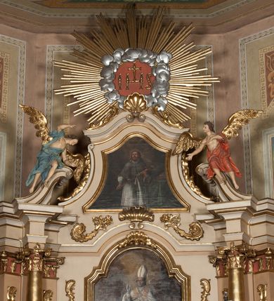 Zdjęcie nr 3: Nastawa ołtarzowa architektoniczna, jednoosiowa z bramkami, jednokondygnacyjna ze zwieńczeniem, na wysokim cokole. Ołtarz prostopadłościenny, mensa drewniana z marmurowym portatylem. Antepedium w formie leżącego prostokąta, ujęte profilowaną ramą. W jego polu trzy medaliony, w środkowym monogram IHS, w zewnętrznych alfa i omega, w narożach rocaille. Tabernakulum w formie prostopadłościennej metalowej skrzynki obitej fakturowaną blachą. Drzwiczki dwuskrzydłowe w kształcie stojącego prostokąta, w metalowych opaskach, z aplikowanymi, odlewanymi przedstawieniami krzyży ze zbożem i winnym gronem na fakturowanym tle. Tabernakulum w drewnianej obudowie stanowiącej dwustrefowy cokół dla tronu wstawienia, dekorowany płycinami z rozetami. Tron w formie obrotowej niszy w kształcie stojącego prostokąta zamkniętego łukiem półkolistym, ujętej dwiema parami kolumienek o kapitelach korynckich, dźwigających pełne belkowanie, przyjmujące nad niszą kształt łuku segmentowego o wypukłym licu. Na belkowaniu cokół ujęty w narożach spływami wolutowymi z figurą baranka apokaliptycznego na księdze.  
Nastawa flankowana dwiema parami pilastrów i parą filarów zewnętrznych ustawionych delikatnie pod kątem względem lica ołtarza, o trzonach dekorowanych rocaille&#039;m i zwisami kwiatowymi, przed nimi para kolumn o kapitelach kompozytowych. Podpory dźwigają pełne belkowanie, wyłamane na ich osi oraz przerwany, wolutowy przyczółek z figurami aniołów. Belkowanie przerwane nad polem środkowym, połączone architrawem przyjmującym kształt łuku nadwieszonego. W polu środkowym nisza w formie stojącego prostokąta zamkniętego łukiem półkolistym nadwieszonym z uskokiem z obrazem św. Stanisława, ujęta profilowaną ramą dekorowaną rocaille&#039;m. Nisza flankowana rocaille&#039;m i zwisami kwiatowymi. Kondygnacja ujęta uszami utworzonymi z rocaille&#039;u, wolut i dekoracji roślinnej. Zwieńczenie w formie zbliżonej do trapezu o wklęsłych bokach, zamknięte gzymsem przechodzącym w dwie zwrócone ku sobie woluty, zakończone medalionem z monogramem IHS w otoku z obłoków, w glorii promienistej. W polu obraz w formie analogicznej względem zwieńczenia z przedstawieniem św. Jana Nepomucena, ujęty w profilowaną ramę. U dołu dekorowany muszlą flankowaną przez ornament roślinny. Bramki z przejściami w formie stojącego prostokąta z nadprożem w kształcie cokołów, utworzonych z dwóch wolut, na których stoją figury św. Stanisława i św. Wojciecha. Struktura polichromowana w kolorze bladoróżowym, kapitele na różowo, ornamentyka, profile i kolumny pozłocone.