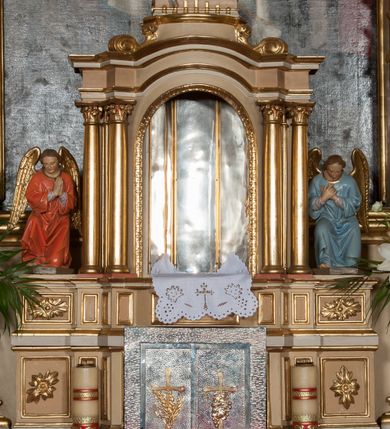 Zdjęcie nr 6: Nastawa ołtarzowa architektoniczna, jednoosiowa z bramkami, jednokondygnacyjna ze zwieńczeniem, na wysokim cokole. Ołtarz prostopadłościenny, mensa drewniana z marmurowym portatylem. Antepedium w formie leżącego prostokąta, ujęte profilowaną ramą. W jego polu trzy medaliony, w środkowym monogram IHS, w zewnętrznych alfa i omega, w narożach rocaille. Tabernakulum w formie prostopadłościennej metalowej skrzynki obitej fakturowaną blachą. Drzwiczki dwuskrzydłowe w kształcie stojącego prostokąta, w metalowych opaskach, z aplikowanymi, odlewanymi przedstawieniami krzyży ze zbożem i winnym gronem na fakturowanym tle. Tabernakulum w drewnianej obudowie stanowiącej dwustrefowy cokół dla tronu wstawienia, dekorowany płycinami z rozetami. Tron w formie obrotowej niszy w kształcie stojącego prostokąta zamkniętego łukiem półkolistym, ujętej dwiema parami kolumienek o kapitelach korynckich, dźwigających pełne belkowanie, przyjmujące nad niszą kształt łuku segmentowego o wypukłym licu. Na belkowaniu cokół ujęty w narożach spływami wolutowymi z figurą baranka apokaliptycznego na księdze.  
Nastawa flankowana dwiema parami pilastrów i parą filarów zewnętrznych ustawionych delikatnie pod kątem względem lica ołtarza, o trzonach dekorowanych rocaille'm i zwisami kwiatowymi, przed nimi para kolumn o kapitelach kompozytowych. Podpory dźwigają pełne belkowanie, wyłamane na ich osi oraz przerwany, wolutowy przyczółek z figurami aniołów. Belkowanie przerwane nad polem środkowym, połączone architrawem przyjmującym kształt łuku nadwieszonego. W polu środkowym nisza w formie stojącego prostokąta zamkniętego łukiem półkolistym nadwieszonym z uskokiem z obrazem św. Stanisława, ujęta profilowaną ramą dekorowaną rocaille'm. Nisza flankowana rocaille'm i zwisami kwiatowymi. Kondygnacja ujęta uszami utworzonymi z rocaille'u, wolut i dekoracji roślinnej. Zwieńczenie w formie zbliżonej do trapezu o wklęsłych bokach, zamknięte gzymsem przechodzącym w dwie zwrócone ku sobie woluty, zakończone medalionem z monogramem IHS w otoku z obłoków, w glorii promienistej. W polu obraz w formie analogicznej względem zwieńczenia z przedstawieniem św. Jana Nepomucena, ujęty w profilowaną ramę. U dołu dekorowany muszlą flankowaną przez ornament roślinny. Bramki z przejściami w formie stojącego prostokąta z nadprożem w kształcie cokołów, utworzonych z dwóch wolut, na których stoją figury św. Stanisława i św. Wojciecha. Struktura polichromowana w kolorze bladoróżowym, kapitele na różowo, ornamentyka, profile i kolumny pozłocone.