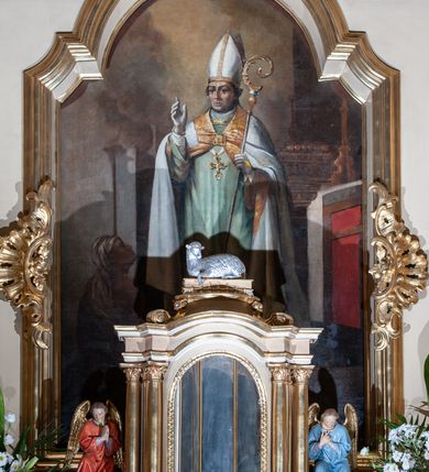 Zdjęcie nr 14: Nastawa ołtarzowa architektoniczna, jednoosiowa z bramkami, jednokondygnacyjna ze zwieńczeniem, na wysokim cokole. Ołtarz prostopadłościenny, mensa drewniana z marmurowym portatylem. Antepedium w formie leżącego prostokąta, ujęte profilowaną ramą. W jego polu trzy medaliony, w środkowym monogram IHS, w zewnętrznych alfa i omega, w narożach rocaille. Tabernakulum w formie prostopadłościennej metalowej skrzynki obitej fakturowaną blachą. Drzwiczki dwuskrzydłowe w kształcie stojącego prostokąta, w metalowych opaskach, z aplikowanymi, odlewanymi przedstawieniami krzyży ze zbożem i winnym gronem na fakturowanym tle. Tabernakulum w drewnianej obudowie stanowiącej dwustrefowy cokół dla tronu wstawienia, dekorowany płycinami z rozetami. Tron w formie obrotowej niszy w kształcie stojącego prostokąta zamkniętego łukiem półkolistym, ujętej dwiema parami kolumienek o kapitelach korynckich, dźwigających pełne belkowanie, przyjmujące nad niszą kształt łuku segmentowego o wypukłym licu. Na belkowaniu cokół ujęty w narożach spływami wolutowymi z figurą baranka apokaliptycznego na księdze.  
Nastawa flankowana dwiema parami pilastrów i parą filarów zewnętrznych ustawionych delikatnie pod kątem względem lica ołtarza, o trzonach dekorowanych rocaille'm i zwisami kwiatowymi, przed nimi para kolumn o kapitelach kompozytowych. Podpory dźwigają pełne belkowanie, wyłamane na ich osi oraz przerwany, wolutowy przyczółek z figurami aniołów. Belkowanie przerwane nad polem środkowym, połączone architrawem przyjmującym kształt łuku nadwieszonego. W polu środkowym nisza w formie stojącego prostokąta zamkniętego łukiem półkolistym nadwieszonym z uskokiem z obrazem św. Stanisława, ujęta profilowaną ramą dekorowaną rocaille'm. Nisza flankowana rocaille'm i zwisami kwiatowymi. Kondygnacja ujęta uszami utworzonymi z rocaille'u, wolut i dekoracji roślinnej. Zwieńczenie w formie zbliżonej do trapezu o wklęsłych bokach, zamknięte gzymsem przechodzącym w dwie zwrócone ku sobie woluty, zakończone medalionem z monogramem IHS w otoku z obłoków, w glorii promienistej. W polu obraz w formie analogicznej względem zwieńczenia z przedstawieniem św. Jana Nepomucena, ujęty w profilowaną ramę. U dołu dekorowany muszlą flankowaną przez ornament roślinny. Bramki z przejściami w formie stojącego prostokąta z nadprożem w kształcie cokołów, utworzonych z dwóch wolut, na których stoją figury św. Stanisława i św. Wojciecha. Struktura polichromowana w kolorze bladoróżowym, kapitele na różowo, ornamentyka, profile i kolumny pozłocone.