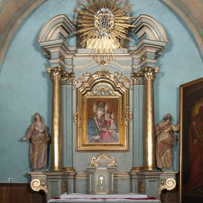 Zdjęcie nr 1: Nastawa architektoniczna, jednoosiowa, jednokondygnacyjna, ustawiona na wysokim cokole. Ołtarz w formie prostopadłościanu o ściętych z przodu narożach z prostokątną, drewnianą mensą, dekorowany trzema płycinami, na froncie monogram Marii ujęty winnym gronem. Na ołtarzu tabernakulum w formie prostopadłościennej skrzynki o ściętych przednich narożach, flankowanej parą pilastrów podtrzymujących gzyms. Drzwiczki w formie stojącego prostokąta zamkniętego półkoliście, ujęte profilowaną ramą, w polu płaskorzeźbiony kielich z hostią. 
Nastawa flankowana parą zwróconych na zewnątrz zdwojonych pilastrów i stojącą przed nimi parą kolumn o kapitelach kompozytowych. Podpory dźwigają pełne belkowanie z wyłamanym nad polem środkowym na kształt łuku odcinkowego gzymsem oraz przerwany, półkolisty przyczółek. Po zewnętrznej stronie kolumn dwie konsole, na których stoją figury św. Anny i św. Joachima. W polu głównym nisza w formie stojącego prostokąta zamkniętego łukiem półkolistym nadwieszonym z uskokiem, ujęta profilowaną ramą, dekorowana rocaille'em, wewnątrz mniejszy obraz Matki Boskiej z Dzieciątkiem w kształcie stojącego prostokąta. W przyłuczach niszy dwie ukwiecone gałązki, na gzymsie uskrzydlona główka anielska, u dołu rocaille'owy kartusz. W miejscu zwieńczenia, na tle okna zamontowany medalion z monogramem Marii w glorii promienistej. Struktura polichromowana w kolorze jasnoniebieskim z beżowymi detalami, ornamentyka, kolumny i profile pozłocone. 