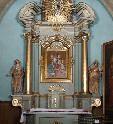 Zdjęcie nr 14: Nastawa architektoniczna, jednoosiowa, jednokondygnacyjna, ustawiona na wysokim cokole. Ołtarz w formie prostopadłościanu o ściętych z przodu narożach z prostokątną, drewnianą mensą, dekorowany trzema płycinami, na froncie monogram Marii ujęty winnym gronem. Na ołtarzu tabernakulum w formie prostopadłościennej skrzynki o ściętych przednich narożach, flankowanej parą pilastrów podtrzymujących gzyms. Drzwiczki w formie stojącego prostokąta zamkniętego półkoliście, ujęte profilowaną ramą, w polu płaskorzeźbiony kielich z hostią. 
Nastawa flankowana parą zwróconych na zewnątrz zdwojonych pilastrów i stojącą przed nimi parą kolumn o kapitelach kompozytowych. Podpory dźwigają pełne belkowanie z wyłamanym nad polem środkowym na kształt łuku odcinkowego gzymsem oraz przerwany, półkolisty przyczółek. Po zewnętrznej stronie kolumn dwie konsole, na których stoją figury św. Anny i św. Joachima. W polu głównym nisza w formie stojącego prostokąta zamkniętego łukiem półkolistym nadwieszonym z uskokiem, ujęta profilowaną ramą, dekorowana rocaille'em, wewnątrz mniejszy obraz Matki Boskiej z Dzieciątkiem w kształcie stojącego prostokąta. W przyłuczach niszy dwie ukwiecone gałązki, na gzymsie uskrzydlona główka anielska, u dołu rocaille'owy kartusz. W miejscu zwieńczenia, na tle okna zamontowany medalion z monogramem Marii w glorii promienistej. Struktura polichromowana w kolorze jasnoniebieskim z beżowymi detalami, ornamentyka, kolumny i profile pozłocone. 