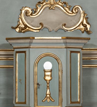 Zdjęcie nr 15: Nastawa architektoniczna, jednoosiowa, jednokondygnacyjna, ustawiona na wysokim cokole. Ołtarz w formie prostopadłościanu o ściętych z przodu narożach z prostokątną, drewnianą mensą, dekorowany trzema płycinami, na froncie monogram Marii ujęty winnym gronem. Na ołtarzu tabernakulum w formie prostopadłościennej skrzynki o ściętych przednich narożach, flankowanej parą pilastrów podtrzymujących gzyms. Drzwiczki w formie stojącego prostokąta zamkniętego półkoliście, ujęte profilowaną ramą, w polu płaskorzeźbiony kielich z hostią. 
Nastawa flankowana parą zwróconych na zewnątrz zdwojonych pilastrów i stojącą przed nimi parą kolumn o kapitelach kompozytowych. Podpory dźwigają pełne belkowanie z wyłamanym nad polem środkowym na kształt łuku odcinkowego gzymsem oraz przerwany, półkolisty przyczółek. Po zewnętrznej stronie kolumn dwie konsole, na których stoją figury św. Anny i św. Joachima. W polu głównym nisza w formie stojącego prostokąta zamkniętego łukiem półkolistym nadwieszonym z uskokiem, ujęta profilowaną ramą, dekorowana rocaille'em, wewnątrz mniejszy obraz Matki Boskiej z Dzieciątkiem w kształcie stojącego prostokąta. W przyłuczach niszy dwie ukwiecone gałązki, na gzymsie uskrzydlona główka anielska, u dołu rocaille'owy kartusz. W miejscu zwieńczenia, na tle okna zamontowany medalion z monogramem Marii w glorii promienistej. Struktura polichromowana w kolorze jasnoniebieskim z beżowymi detalami, ornamentyka, kolumny i profile pozłocone. 