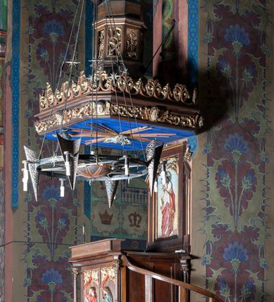 Zdjęcie nr 2: Ambona stojąca, usytuowana przy filarze z dostępem schodami z prawej strony, ustawiona na czworościennym filarze. Filar osadzony jest na szerokiej plincie i węższej bazie; trzon podzielony jest na dwie części. Poszczególne partie trzonu oddzielone są od siebie gzymsami. Naroża dolnej części artykułowane są filarkami ustawionymi na wysokich cokołach, a ścianki filarów dekorowane są neogotyckimi płycinami, zakończonymi motywem dwuliścia. Ścianki dolnej części cokołu zdobione są podwójnymi blendami. Górna część trzonu jest niższa, w narożach artykułowana pinaklami o szczytach wywiniętych do przodu. Na ściankach kwadratowe płyciny wypełnione rzeźbioną i złoconą dekoracją roślinną. Nad tą częścią trzonu osadzony jest ścięty ostrosłup czworokątny, na którym wspiera się kosz ambony. Ścianki ostrosłupa wypełnione są rzeźbionymi atrybutami ewangelistów przedstawiającymi im odpowiednio: anioła, lwa, orła i woła.

Kosz ambony założony jest na planie kwadratu, naroża flankują wąskie kolumienki wspierające niepełne belkowanie i parapet. Bazy kolumienek wysokie, sześcioboczne, wyżej zdobione rzeźbioną plecionką; trzony gładkie, kapitele zdobione motywami neogotyckimi. Na lewej i środkowej ściance kosza umieszczono po dwie prostokątne płyciny z rzeźbionymi przedstawieniami ewangelistów. Kompozycje zamknięte w profilowanych ramach w kształcie stojących prostokątów, zamkniętych oślim grzbietem i motywem akantu rozchodzącym się od niego symetrycznie na przyłucza. Ewangeliści ukazani są w pozycji siedzącej z księgami w dłoniach. Ubrani są w różnokolorowe suknie z długimi rękawami i płaszcze o złoconej bordiurze. Twarze szczupłe, okolone brodami i bujnymi oraz silnie skręconymi włosami. 

Zaplecek prostokątny, w polu w prostokątnej płycinie płaskorzeźba Chrystusa Dobrego Pasterza, u góry dekoracja złożona z astwerku i liści akantu. Baldachim na planie kwadratu o ściętych narożach. Podniebienie polichromowane na kolor ciemnoniebieski z rzeźbioną gołębicą Ducha Świętego w polu na tle promienistej glorii złożonej z wiązek promieni o nierównej długości. Fryz belkowania zdobią uskrzydlone główki aniołków, skierowane na wprost oraz dekoracja roślinna, nad belkowaniem biegnie rzeźbiony pas ażurowej koronki w kształcie wici roślinnej. Na baldachimie ośmioboczny cokół z otworami w kształcie stojących prostokątów wypełnionych ażurowym ornamentem roślinnym. Na cokole ustawiona jest ośmioboczna podstawa o uskokowej górnej części, na które stoi pełnoplastyczna figura Chrystusa Zmartwychwstałego, ubranego w czerwony płaszcz, który w lewej dłoni trzyma chorągiew, a prawą unosi do góry. Jego twarz jest podłużna, okolona zarostem, włosy długie, kręcone i bujne, a wokół głowy ma promienisty nimb. Schody z poręczą i prostymi tralkami, bez zdobień. Ambona w kolorze naturalnego drewna, ornamentyka złocona, detale srebrzone i złocone, podniebienie baldachimu polichromowane na kolor ciemnoniebieski. 
