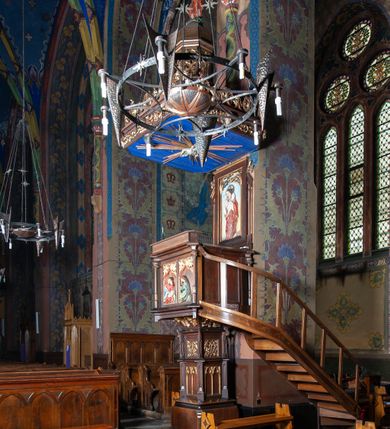 Zdjęcie nr 1: Ambona stojąca, usytuowana przy filarze z dostępem schodami z prawej strony, ustawiona na czworościennym filarze. Filar osadzony jest na szerokiej plincie i węższej bazie; trzon podzielony jest na dwie części. Poszczególne partie trzonu oddzielone są od siebie gzymsami. Naroża dolnej części artykułowane są filarkami ustawionymi na wysokich cokołach, a ścianki filarów dekorowane są neogotyckimi płycinami, zakończonymi motywem dwuliścia. Ścianki dolnej części cokołu zdobione są podwójnymi blendami. Górna część trzonu jest niższa, w narożach artykułowana pinaklami o szczytach wywiniętych do przodu. Na ściankach kwadratowe płyciny wypełnione rzeźbioną i złoconą dekoracją roślinną. Nad tą częścią trzonu osadzony jest ścięty ostrosłup czworokątny, na którym wspiera się kosz ambony. Ścianki ostrosłupa wypełnione są rzeźbionymi atrybutami ewangelistów przedstawiającymi im odpowiednio: anioła, lwa, orła i woła.

Kosz ambony założony jest na planie kwadratu, naroża flankują wąskie kolumienki wspierające niepełne belkowanie i parapet. Bazy kolumienek wysokie, sześcioboczne, wyżej zdobione rzeźbioną plecionką; trzony gładkie, kapitele zdobione motywami neogotyckimi. Na lewej i środkowej ściance kosza umieszczono po dwie prostokątne płyciny z rzeźbionymi przedstawieniami ewangelistów. Kompozycje zamknięte w profilowanych ramach w kształcie stojących prostokątów, zamkniętych oślim grzbietem i motywem akantu rozchodzącym się od niego symetrycznie na przyłucza. Ewangeliści ukazani są w pozycji siedzącej z księgami w dłoniach. Ubrani są w różnokolorowe suknie z długimi rękawami i płaszcze o złoconej bordiurze. Twarze szczupłe, okolone brodami i bujnymi oraz silnie skręconymi włosami. 

Zaplecek prostokątny, w polu w prostokątnej płycinie płaskorzeźba Chrystusa Dobrego Pasterza, u góry dekoracja złożona z astwerku i liści akantu. Baldachim na planie kwadratu o ściętych narożach. Podniebienie polichromowane na kolor ciemnoniebieski z rzeźbioną gołębicą Ducha Świętego w polu na tle promienistej glorii złożonej z wiązek promieni o nierównej długości. Fryz belkowania zdobią uskrzydlone główki aniołków, skierowane na wprost oraz dekoracja roślinna, nad belkowaniem biegnie rzeźbiony pas ażurowej koronki w kształcie wici roślinnej. Na baldachimie ośmioboczny cokół z otworami w kształcie stojących prostokątów wypełnionych ażurowym ornamentem roślinnym. Na cokole ustawiona jest ośmioboczna podstawa o uskokowej górnej części, na które stoi pełnoplastyczna figura Chrystusa Zmartwychwstałego, ubranego w czerwony płaszcz, który w lewej dłoni trzyma chorągiew, a prawą unosi do góry. Jego twarz jest podłużna, okolona zarostem, włosy długie, kręcone i bujne, a wokół głowy ma promienisty nimb. Schody z poręczą i prostymi tralkami, bez zdobień. Ambona w kolorze naturalnego drewna, ornamentyka złocona, detale srebrzone i złocone, podniebienie baldachimu polichromowane na kolor ciemnoniebieski. 
