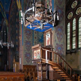 Zdjęcie nr 1: Ambona stojąca, usytuowana przy filarze z dostępem schodami z prawej strony, ustawiona na czworościennym filarze. Filar osadzony jest na szerokiej plincie i węższej bazie; trzon podzielony jest na dwie części. Poszczególne partie trzonu oddzielone są od siebie gzymsami. Naroża dolnej części artykułowane są filarkami ustawionymi na wysokich cokołach, a ścianki filarów dekorowane są neogotyckimi płycinami, zakończonymi motywem dwuliścia. Ścianki dolnej części cokołu zdobione są podwójnymi blendami. Górna część trzonu jest niższa, w narożach artykułowana pinaklami o szczytach wywiniętych do przodu. Na ściankach kwadratowe płyciny wypełnione rzeźbioną i złoconą dekoracją roślinną. Nad tą częścią trzonu osadzony jest ścięty ostrosłup czworokątny, na którym wspiera się kosz ambony. Ścianki ostrosłupa wypełnione są rzeźbionymi atrybutami ewangelistów przedstawiającymi im odpowiednio: anioła, lwa, orła i woła.

Kosz ambony założony jest na planie kwadratu, naroża flankują wąskie kolumienki wspierające niepełne belkowanie i parapet. Bazy kolumienek wysokie, sześcioboczne, wyżej zdobione rzeźbioną plecionką; trzony gładkie, kapitele zdobione motywami neogotyckimi. Na lewej i środkowej ściance kosza umieszczono po dwie prostokątne płyciny z rzeźbionymi przedstawieniami ewangelistów. Kompozycje zamknięte w profilowanych ramach w kształcie stojących prostokątów, zamkniętych oślim grzbietem i motywem akantu rozchodzącym się od niego symetrycznie na przyłucza. Ewangeliści ukazani są w pozycji siedzącej z księgami w dłoniach. Ubrani są w różnokolorowe suknie z długimi rękawami i płaszcze o złoconej bordiurze. Twarze szczupłe, okolone brodami i bujnymi oraz silnie skręconymi włosami. 

Zaplecek prostokątny, w polu w prostokątnej płycinie płaskorzeźba Chrystusa Dobrego Pasterza, u góry dekoracja złożona z astwerku i liści akantu. Baldachim na planie kwadratu o ściętych narożach. Podniebienie polichromowane na kolor ciemnoniebieski z rzeźbioną gołębicą Ducha Świętego w polu na tle promienistej glorii złożonej z wiązek promieni o nierównej długości. Fryz belkowania zdobią uskrzydlone główki aniołków, skierowane na wprost oraz dekoracja roślinna, nad belkowaniem biegnie rzeźbiony pas ażurowej koronki w kształcie wici roślinnej. Na baldachimie ośmioboczny cokół z otworami w kształcie stojących prostokątów wypełnionych ażurowym ornamentem roślinnym. Na cokole ustawiona jest ośmioboczna podstawa o uskokowej górnej części, na które stoi pełnoplastyczna figura Chrystusa Zmartwychwstałego, ubranego w czerwony płaszcz, który w lewej dłoni trzyma chorągiew, a prawą unosi do góry. Jego twarz jest podłużna, okolona zarostem, włosy długie, kręcone i bujne, a wokół głowy ma promienisty nimb. Schody z poręczą i prostymi tralkami, bez zdobień. Ambona w kolorze naturalnego drewna, ornamentyka złocona, detale srebrzone i złocone, podniebienie baldachimu polichromowane na kolor ciemnoniebieski. 
