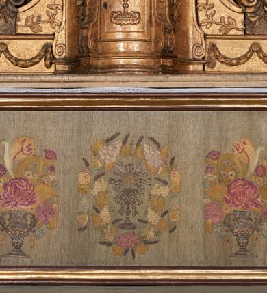 Zdjęcie nr 6: Ołtarz kamienny, prostopadłościenny, z kamienną mensą oraz antepedium w formie leżącego prostokąta z tkaniny, ujętym profilowaną, drewnianą i złoconą ramą. Na ołtarzu ustawione tabernakulum z tronem wystawienia. 
Nastawa architektoniczna, jednoosiowa, jednokondygnacyjna ze zwieńczeniem, ustawiona na dwustrefowym cokole ze skrajnie wyłamanymi pod kątem trzema parami prostopadłościanów. Retabulum ujęte ustawionymi pod kątem na zewnątrz filarami, opilastrowanymi po wewnętrznej stronie oraz stojącą przed nimi parą kolumn o kapitelach kompozytowych. Na skrajnie wyłamanych fragmentach cokołu ustawione figury świętego biskupa i świętego papieża. Podpory dźwigają pełne belkowanie połączone nad polem głównym wyłącznie gzymsem wyłamanym na kształt łuku odcinkowego nadwieszonego. Na osi kolumn, na belkowaniu fragmenty przerwanego falistego przyczółka, skierowane do wewnątrz, na których znajdują się dwie figury siedzących aniołów. W polu głównym wnęka w formie stojącego prostokąta zamkniętego łukiem półkolistym nadwieszonym z uskokiem, ujęta profilowaną ramą dekorowaną rocaille'm. W niej zamontowany obraz Trójcy Świętej ze św. Franciszkiem i św. Dominikiem. Ponad wnęką rokokowy kartusz z napisem w polu: „S[anctus] S[anctus] S[anctus]”. Po bokach wnęki dwa pola w kształcie rombów o ściętych kątach z wprawionymi lustrami. Zwieńczenie w formie zbliżonej do trapezu ujętego spływami wolutowymi, zamkniętego fragmentem falistego gzymsu, dekorowane z trzech stron rocaille'm. W polu zwieńczenia płycina o tej samej formie, wewnątrz obraz św. Marii Magdaleny w kształcie zbliżonym do trapezu o ściętych dolnych narożach, ujęty profilowaną ramą dekorowaną rocaille'm. Struktura polichromowana w odcieniach beżu, partiami zaś różu i jasnej czerwieni; płyciny cokołu i trzony kolumn polichromowane na sposób imitujący marmoryzację w odcieniach zieleni, niektóre płyciny również czerwieni. Profile i ornamentyka złocone.
