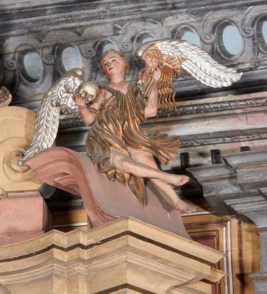 Zdjęcie nr 9: Ołtarz kamienny, prostopadłościenny, z kamienną mensą oraz antepedium w formie leżącego prostokąta z tkaniny, ujętym profilowaną, drewnianą i złoconą ramą. Na ołtarzu ustawione tabernakulum z tronem wystawienia. 
Nastawa architektoniczna, jednoosiowa, jednokondygnacyjna ze zwieńczeniem, ustawiona na dwustrefowym cokole ze skrajnie wyłamanymi pod kątem trzema parami prostopadłościanów. Retabulum ujęte ustawionymi pod kątem na zewnątrz filarami, opilastrowanymi po wewnętrznej stronie oraz stojącą przed nimi parą kolumn o kapitelach kompozytowych. Na skrajnie wyłamanych fragmentach cokołu ustawione figury świętego biskupa i świętego papieża. Podpory dźwigają pełne belkowanie połączone nad polem głównym wyłącznie gzymsem wyłamanym na kształt łuku odcinkowego nadwieszonego. Na osi kolumn, na belkowaniu fragmenty przerwanego falistego przyczółka, skierowane do wewnątrz, na których znajdują się dwie figury siedzących aniołów. W polu głównym wnęka w formie stojącego prostokąta zamkniętego łukiem półkolistym nadwieszonym z uskokiem, ujęta profilowaną ramą dekorowaną rocaille'm. W niej zamontowany obraz Trójcy Świętej ze św. Franciszkiem i św. Dominikiem. Ponad wnęką rokokowy kartusz z napisem w polu: „S[anctus] S[anctus] S[anctus]”. Po bokach wnęki dwa pola w kształcie rombów o ściętych kątach z wprawionymi lustrami. Zwieńczenie w formie zbliżonej do trapezu ujętego spływami wolutowymi, zamkniętego fragmentem falistego gzymsu, dekorowane z trzech stron rocaille'm. W polu zwieńczenia płycina o tej samej formie, wewnątrz obraz św. Marii Magdaleny w kształcie zbliżonym do trapezu o ściętych dolnych narożach, ujęty profilowaną ramą dekorowaną rocaille'm. Struktura polichromowana w odcieniach beżu, partiami zaś różu i jasnej czerwieni; płyciny cokołu i trzony kolumn polichromowane na sposób imitujący marmoryzację w odcieniach zieleni, niektóre płyciny również czerwieni. Profile i ornamentyka złocone.
