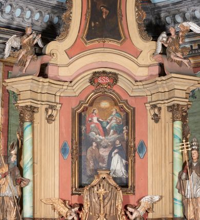 Zdjęcie nr 5: Ołtarz kamienny, prostopadłościenny, z kamienną mensą oraz antepedium w formie leżącego prostokąta z tkaniny, ujętym profilowaną, drewnianą i złoconą ramą. Na ołtarzu ustawione tabernakulum z tronem wystawienia. 
Nastawa architektoniczna, jednoosiowa, jednokondygnacyjna ze zwieńczeniem, ustawiona na dwustrefowym cokole ze skrajnie wyłamanymi pod kątem trzema parami prostopadłościanów. Retabulum ujęte ustawionymi pod kątem na zewnątrz filarami, opilastrowanymi po wewnętrznej stronie oraz stojącą przed nimi parą kolumn o kapitelach kompozytowych. Na skrajnie wyłamanych fragmentach cokołu ustawione figury świętego biskupa i świętego papieża. Podpory dźwigają pełne belkowanie połączone nad polem głównym wyłącznie gzymsem wyłamanym na kształt łuku odcinkowego nadwieszonego. Na osi kolumn, na belkowaniu fragmenty przerwanego falistego przyczółka, skierowane do wewnątrz, na których znajdują się dwie figury siedzących aniołów. W polu głównym wnęka w formie stojącego prostokąta zamkniętego łukiem półkolistym nadwieszonym z uskokiem, ujęta profilowaną ramą dekorowaną rocaille'm. W niej zamontowany obraz Trójcy Świętej ze św. Franciszkiem i św. Dominikiem. Ponad wnęką rokokowy kartusz z napisem w polu: „S[anctus] S[anctus] S[anctus]”. Po bokach wnęki dwa pola w kształcie rombów o ściętych kątach z wprawionymi lustrami. Zwieńczenie w formie zbliżonej do trapezu ujętego spływami wolutowymi, zamkniętego fragmentem falistego gzymsu, dekorowane z trzech stron rocaille'm. W polu zwieńczenia płycina o tej samej formie, wewnątrz obraz św. Marii Magdaleny w kształcie zbliżonym do trapezu o ściętych dolnych narożach, ujęty profilowaną ramą dekorowaną rocaille'm. Struktura polichromowana w odcieniach beżu, partiami zaś różu i jasnej czerwieni; płyciny cokołu i trzony kolumn polichromowane na sposób imitujący marmoryzację w odcieniach zieleni, niektóre płyciny również czerwieni. Profile i ornamentyka złocone.
