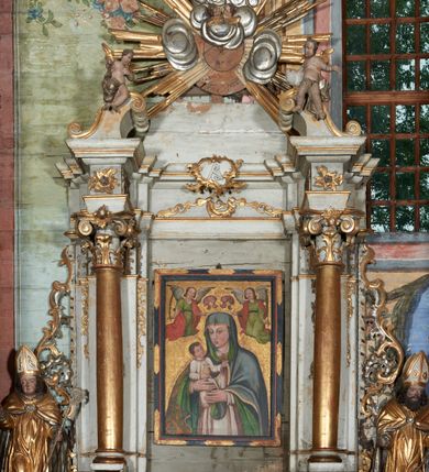 Zdjęcie nr 2: Mensa drewniana; ołtarz sarkofagowy, o wklęsłych bokach, zwężających się ku dołowi, ustawiony na niskim cokole zakończonym podwójnym półwałkiem, dekorowany rocaille'owym kartuszem. Ołtarz ustawiony na trzech drewnianych stopniach.
Retabulum jednoosiowe, jednokondygnacyjne, z niskim dwustrefowym cokołem z wyłamanymi dwoma sześcianami, stanowiącymi cokoły. Nastawa ołtarzowa ujęta parą kolumn kompozytowych ustawionych na tle zwielokrotnionych pilastrów. Podpory wspierają pełne belkowanie z wyłamanymi impostami na osi kolumn, na których znajdują się fragmenty wolutowego przerwanego przyczółka, na których siedzą dwa putta. Zwieńczenie ułamane, nad nim zamontowana gloria promienista z obłokami i dwiema uskrzydlonymi główkami anielskimi. W polu środkowym obraz w formie stojącego prostokąta z przedstawieniem Matki Boskiej z Dzieciątkiem. Nastawa dekorowana ornamentem o motywach roślinnych i cęgowych w partii cokołu, pilastrów i belkowania, na impostach dwie rozety. Retabulum ujęte uszami utworzonymi z ornamentu rocaille'owego i motywów roślinnych. Po bokach ołtarza dostawione cokoły, na których ustawione figury św. Wojciecha i św. Stanisława. Struktura nastawy polichromowana w kolorze białym, profile, kolumny, gloria i ornamentyka złocone.

