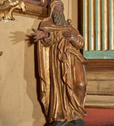 Zdjęcie nr 2: Figura nieopracowana od tyłu; ustawiona na niskiej, nieregularnej podstawie. Święty ukazany frontalnie, z głową przechyloną na lewe ramię, z ugiętą lewą nogą, prawą rękę wyciąga w bok, lewą kładzie na piersi. Twarz ma pociągłą, o niskim czole, niewielkich, wąskich oczach, dużym nosie, pełnych ustach, okoloną długą, falowaną brodą. Ubrany jest w złoconą tunikę przepasaną w talii oraz złocony płaszcz zarzucony na ramiona i głowę, zapięty na lewym ramieniu klamrą w formie kuli, z połą płaszcza podtrzymywaną z przodu postaci. Polichromia ciała naturalistyczna, szaty złocone.

