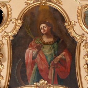 Zdjęcie nr 1: Obraz w formie stojącego prostokąta o wklęsłych bokach, zamkniętego łukiem półkolistym z uskokiem, ujęty profilowaną, złoconą ramą, dekorowaną fragmentami rocaille'u.
W centrum św. Katarzyna ukazana do kolan, frontalnie, z uniesioną głową, skierowaną w prawo. W prawej, ugiętej i uniesionej ręce trzyma liść palmy; lewą, delikatnie opuszczaną przytrzymuje przy boku księgę i dłonią ujmuje rękojeść miecza zwróconego ostrzem w dół. Twarz ma owalną, o pełnych policzkach, o dużych oczach skierowanych w górę, prostym nosie i pełnych ustach. Włosy ma długie, częściowo upięte z tyłu głowy i opadające na plecy. Postać ubrana w białą suknię spodnią, której bufiaste rękawy widoczne są spod płaszcza, jasnozieloną suknię wierzchnią, z zakładką na piersi i brązową tkaniną wokół dekoltu. Na plecy i ramiona ma zarzucony jasnoczerwony, obficie fałdowany płaszcz. Na głowie ma koronę otwartą. Przy jej prawym boku znajduje się ułamane koło obite metalem. Święta ukazana na cieniowanym, brunatnym tle, z wiązką światła padającego z góry na jej głowę.

