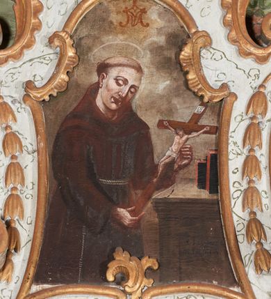 Zdjęcie nr 1: Obraz w formie stojącego prostokąta o wklęsłych bokach, zamknięty łukiem odcinkowym z uskokiem. W centrum obrazu święty ukazany do kolan, zwrócony w trzech czwartych w lewo, z pochyloną głową, obiema rekami podtrzymuje krucyfiks. Twarz ma owalną, o rysunkowo potraktowanych rysach, prostych brwiach, okrągłych oczach skierowanych w dół, prostym, wąskim nosie i pełnych ustach. Włosy krótkie, z tonsurą na głowie. Ubrany jest w ciemnobrązowy habit z kapturem, przepasany w talii podwójnym sznurem. Nad głową świętego nimb. Przed świętym ukazany brązowo-szary mebel o profilowanej krawędzi, na którym stoją dwie książki. Postać ukazana na tle szarych, spiętrzonych obłoków, rozjaśnionych żółcienią w górnej partii obrazu, gdzie ukazany jest monogram Marii. Na meblu widnieje czarny napis „S. JOANNES / DE DUKLA”. 


