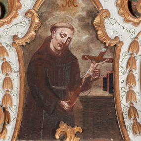 Zdjęcie nr 1: Obraz w formie stojącego prostokąta o wklęsłych bokach, zamknięty łukiem odcinkowym z uskokiem. W centrum obrazu święty ukazany do kolan, zwrócony w trzech czwartych w lewo, z pochyloną głową, obiema rekami podtrzymuje krucyfiks. Twarz ma owalną, o rysunkowo potraktowanych rysach, prostych brwiach, okrągłych oczach skierowanych w dół, prostym, wąskim nosie i pełnych ustach. Włosy krótkie, z tonsurą na głowie. Ubrany jest w ciemnobrązowy habit z kapturem, przepasany w talii podwójnym sznurem. Nad głową świętego nimb. Przed świętym ukazany brązowo-szary mebel o profilowanej krawędzi, na którym stoją dwie książki. Postać ukazana na tle szarych, spiętrzonych obłoków, rozjaśnionych żółcienią w górnej partii obrazu, gdzie ukazany jest monogram Marii. Na meblu widnieje czarny napis „S. JOANNES / DE DUKLA”. 


