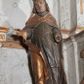 Zdjęcie nr 1: Figura nieopracowana z tyłu; ustawiona na niskiej nieregularnej podstawie. Święty ukazany frontalnie z ugiętą prawą nogą i rękami zgiętymi w łokciach, w tym prawą wyciągniętą w bok z dłonią w geście błogosławieństwa. Twarz ma owalną o prostokątnej żuchwie, niewielkich oczach, krótkim, prostym nosie i małych ustach, okoloną krótkimi włosami skręconymi w pukle. Na głowie ma złoconą infułę z dwoma taśmami. Ubrany jest w albę, rokietę i mucet polichromowane w kolorze ciemnego brązu. Na ramiona ma narzuconą złoconą kapę, zapiętą klamrą w formie czworoliścia, zawiniętą z przodu, na prawej nodze. Na stopie ma but, a na dłoni złoconą rękawiczkę. Polichromia naturalistyczna w odsłoniętych partiach ciała, niektóre elementy stroju złocone (infułą, kapa, rękawiczka).





