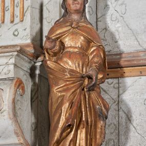 Zdjęcie nr 1: Figura nieopracowana z tyłu; ustawiona na niskiej, nieregularnej podstawie. Święty ukazany frontalnie, prawą, ugiętą rękę wyciąga w bok, lewą, opuszczoną podtrzymuję połę płaszcza. Twarz ma pociągłą, o kwadratowej żuchwie i niskim czole, niewielkich oczach, krótkim, wąskim nosie i małych ustach, okoloną falowanymi włosami opadającymi na ramiona. Ubrany jest w złoconą tunikę przepasaną w talii oraz złocony płaszcz zarzucony na ramiona, zapięty pod szyją klamrą, z połami podtrzymywanymi z przodu postaci. Polichromia ciała naturalistyczna, szaty złocone.


