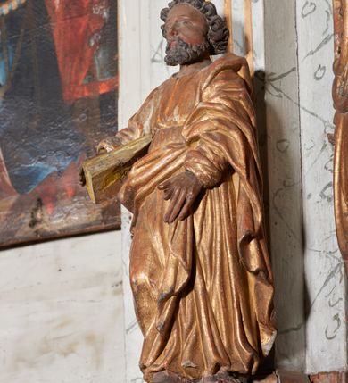 Zdjęcie nr 2: Figura nieopracowana z tyłu; ustawiona na niskiej, nieregularnej podstawie. Święty ukazany frontalnie, z prawą nogą ugiętą, obie ręce wyciąga wprzód, w prawej przytrzymuje księgę. Twarz ma pociągłą, o niewielkich, wąskich oczach, krótkim nosie i małych ustach, okoloną krótkimi, silnie kręconymi włosami i brodą. Ubrany jest w obficie fałdowaną tunikę przepasaną w talii oraz płaszcz zarzucony na lewe ramię i zawinięty z przodu postaci. Polichromia ciała naturalistyczna, szaty złocone. 